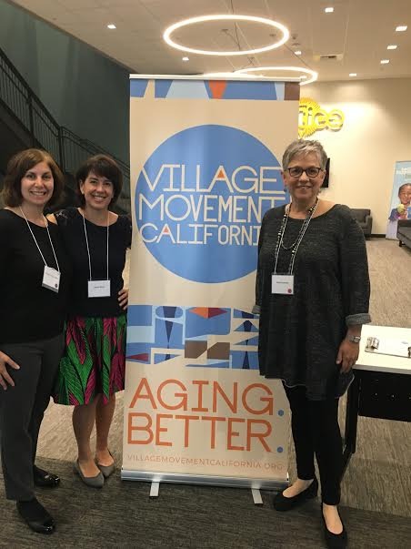 Three women standing beside a Village Movement California banner reading