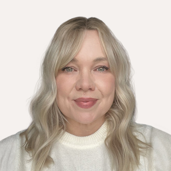 Amy, a white woman with blonde hair wearing a ring-necked white shirt, smiles at the camera.