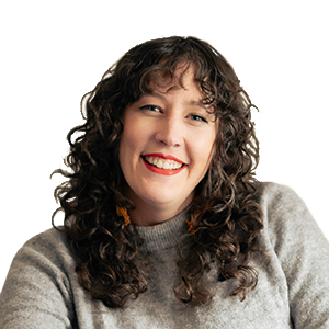 Alyssa, a white woman with curly brown hair, smiles at the camera. She is wearing a grey long sleeved turtleneck and red lipstick