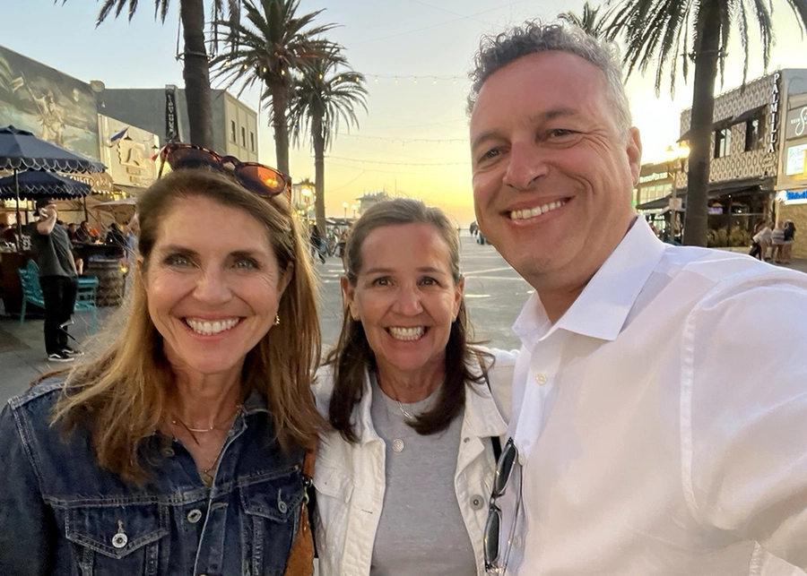 Three colleagues smiling together during an outdoor community event.