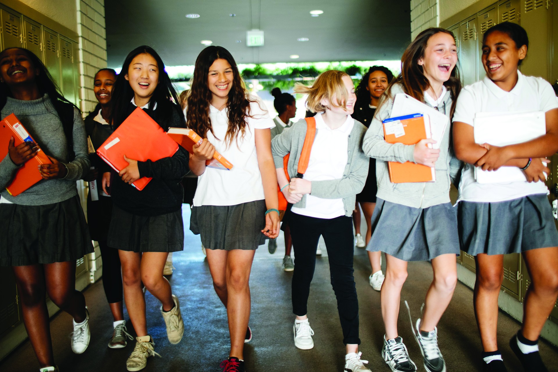 A group of students in uniforms walking and laughing in a school hallway lined with lockers