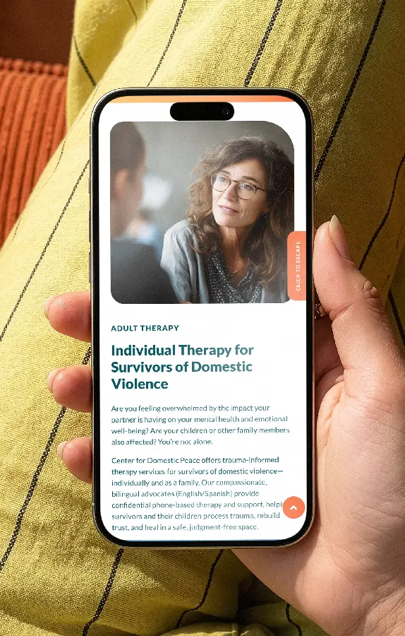 A hand holds a smartphone displaying a Center for Domestic Peace webpage titled "Individual Therapy for Survivors of Domestic Violence," with a photo of a woman and a "Click to Escape" safety button along the screen edge.